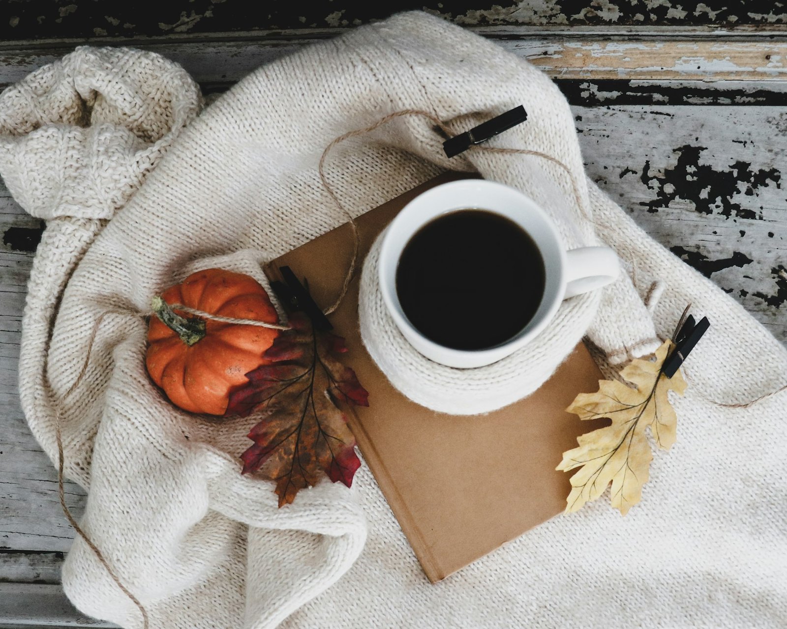 Taza de café y calabaza pequeña sobre una manta de punto blanca